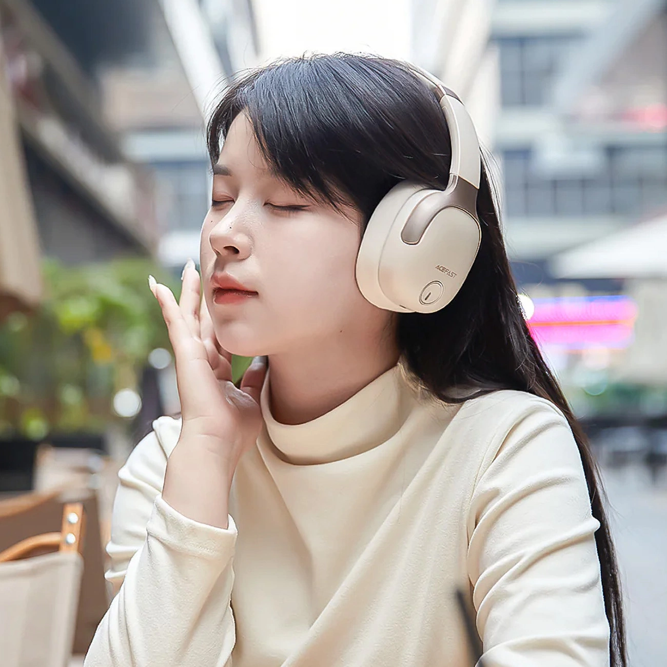 A woman in the garden of a cafe listening to music on Acefast H2 headphones