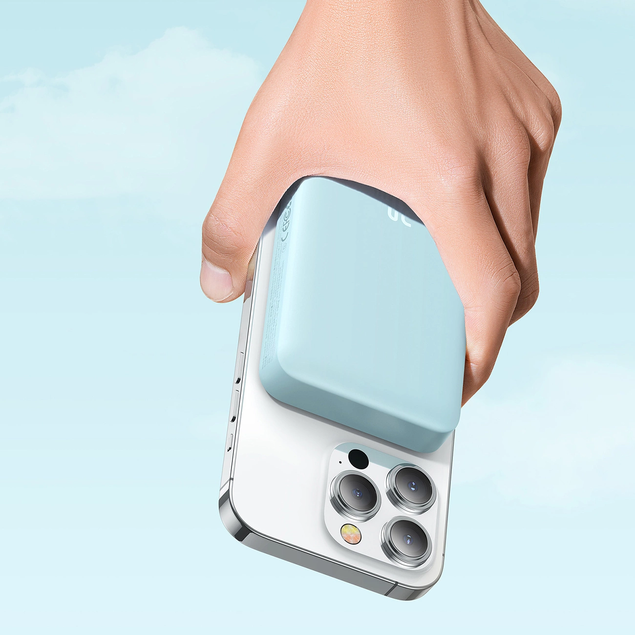 A hand holding a phone with a Baseus Magnetic Mini induction Powerbank 10000mAh 30W attached against the background of clouds