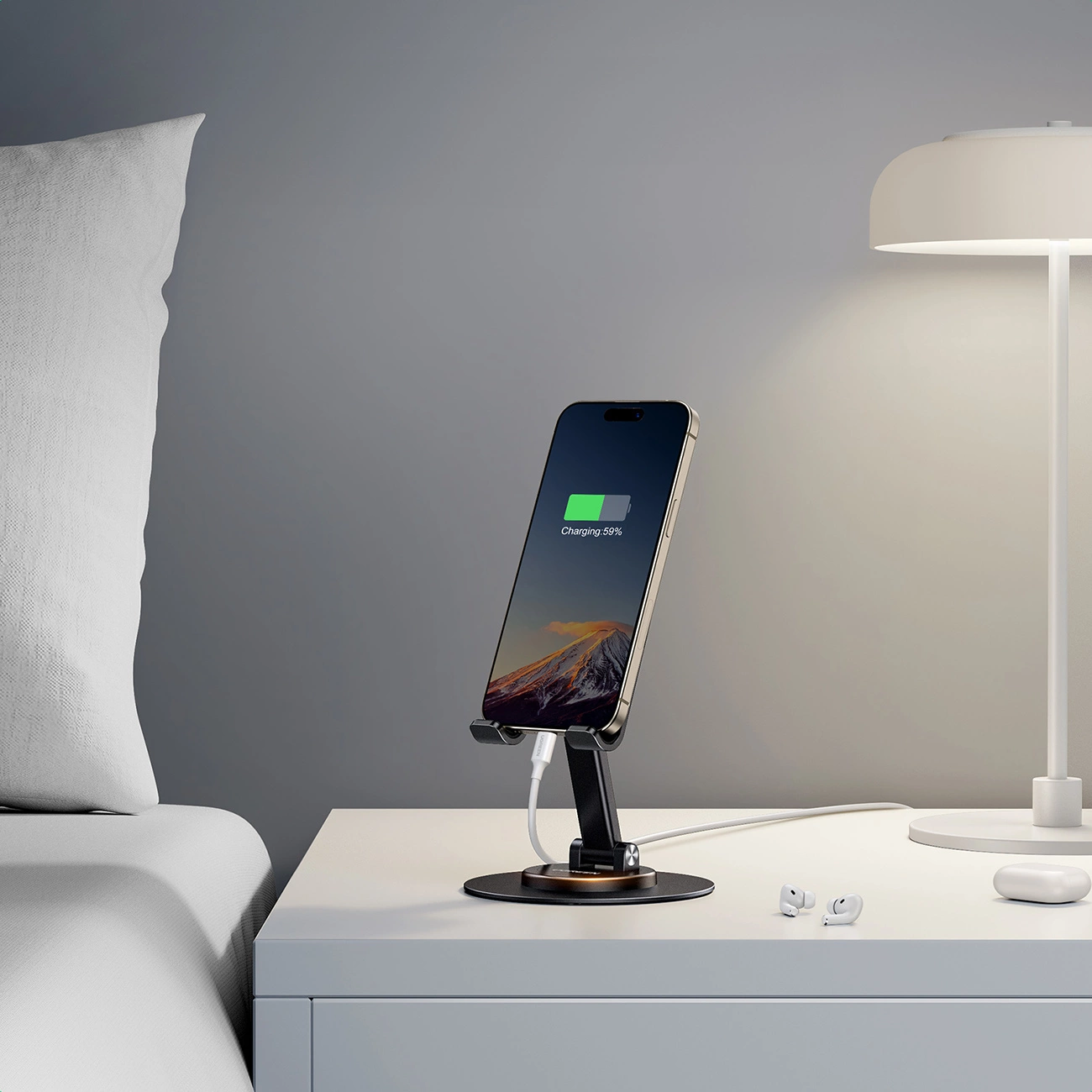 Ugreen LP805 desk stand on a bedside lamp next to the bed. There is a phone on the stand, connected to charging with a white cable.