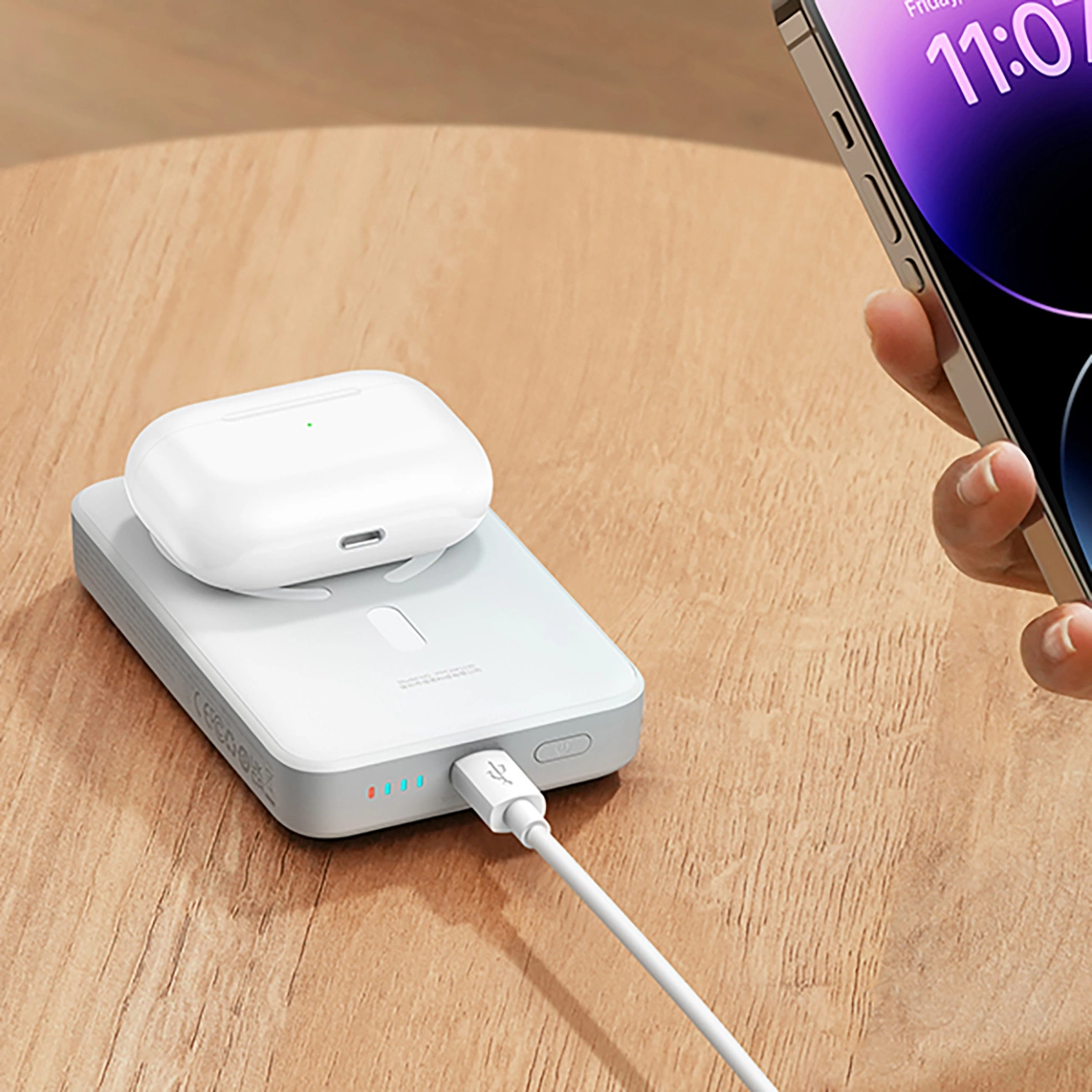 Baseus Magnetic Mini inductive 10000mAh 30W Powerbank lying on a wooden table to which the phone is connected via a cable, and inductively charging headphones lie on the surface of the Baseus Magnetic Mini Powerbank.