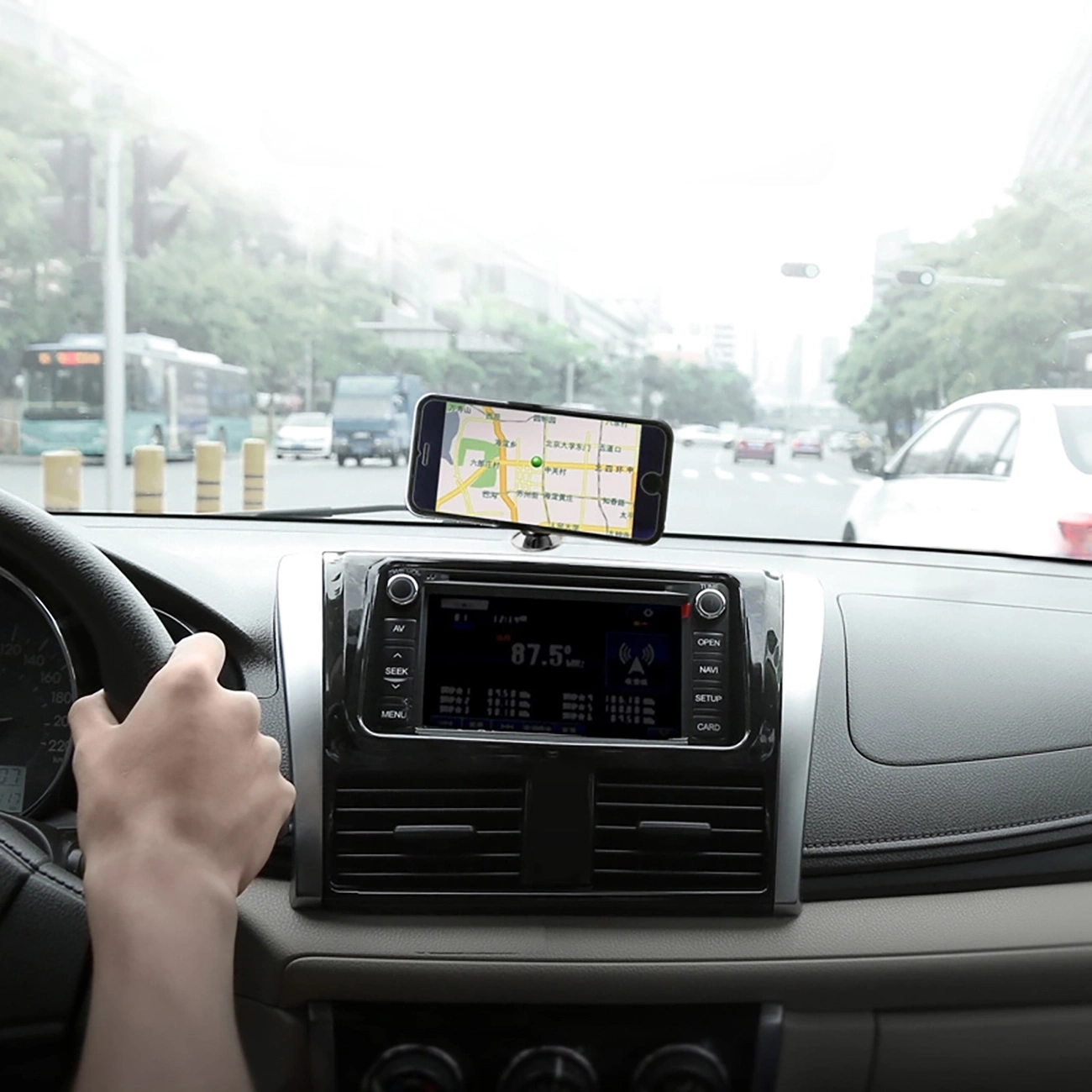 Der Fahrer des Fahrzeugs schaut auf die Navigation auf dem Telefon, das an der am Armaturenbrett befestigten magnetischen Autohalterung Baseus Small Ears Series SUER-A01 befestigt ist