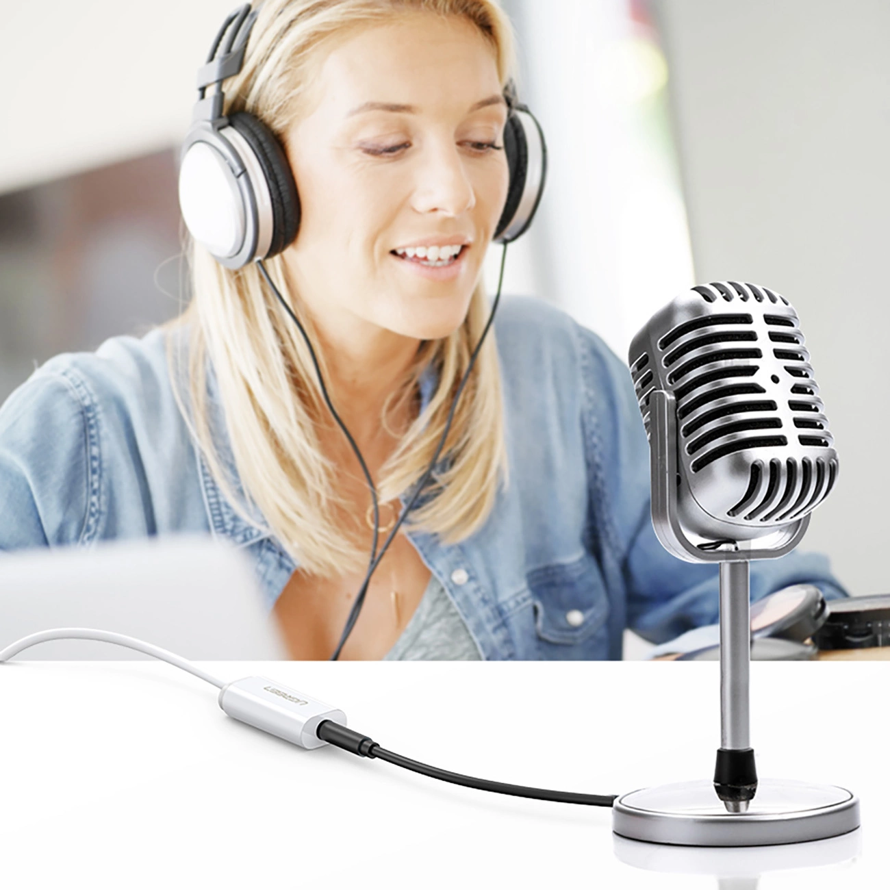 A woman in headphones singing into a microphone connected to the Ugreen US206 audio adapter