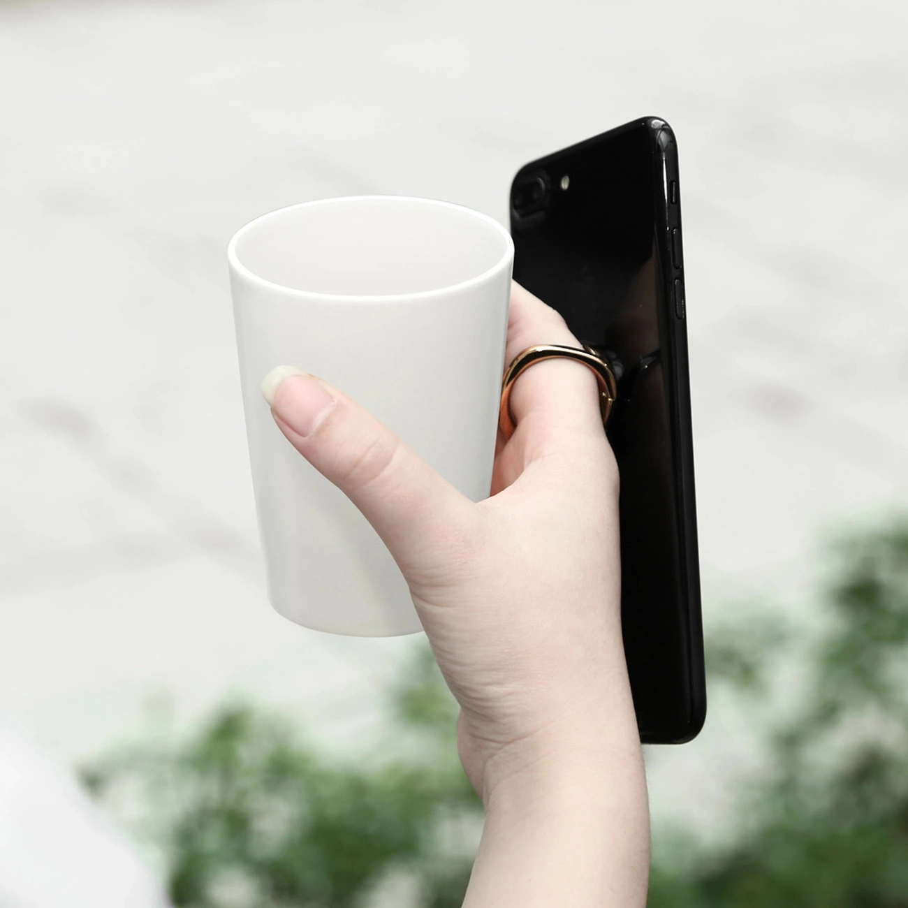 A hand holding a cup and the Baseus Privity Ring holder to which the phone is attached