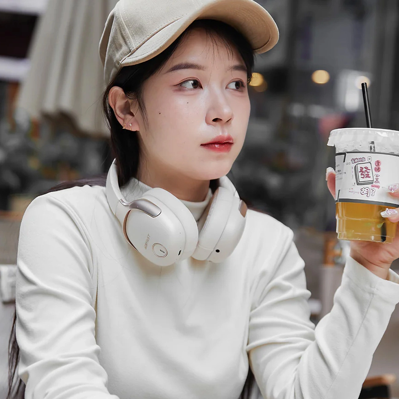 Woman wearing Acefast H2 headphones holding iced tea in a cup with a straw
