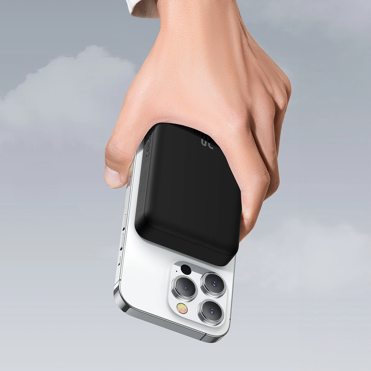 A hand holding a phone with a Baseus Magnetic Mini induction Powerbank 10000mAh 30W attached against the background of clouds