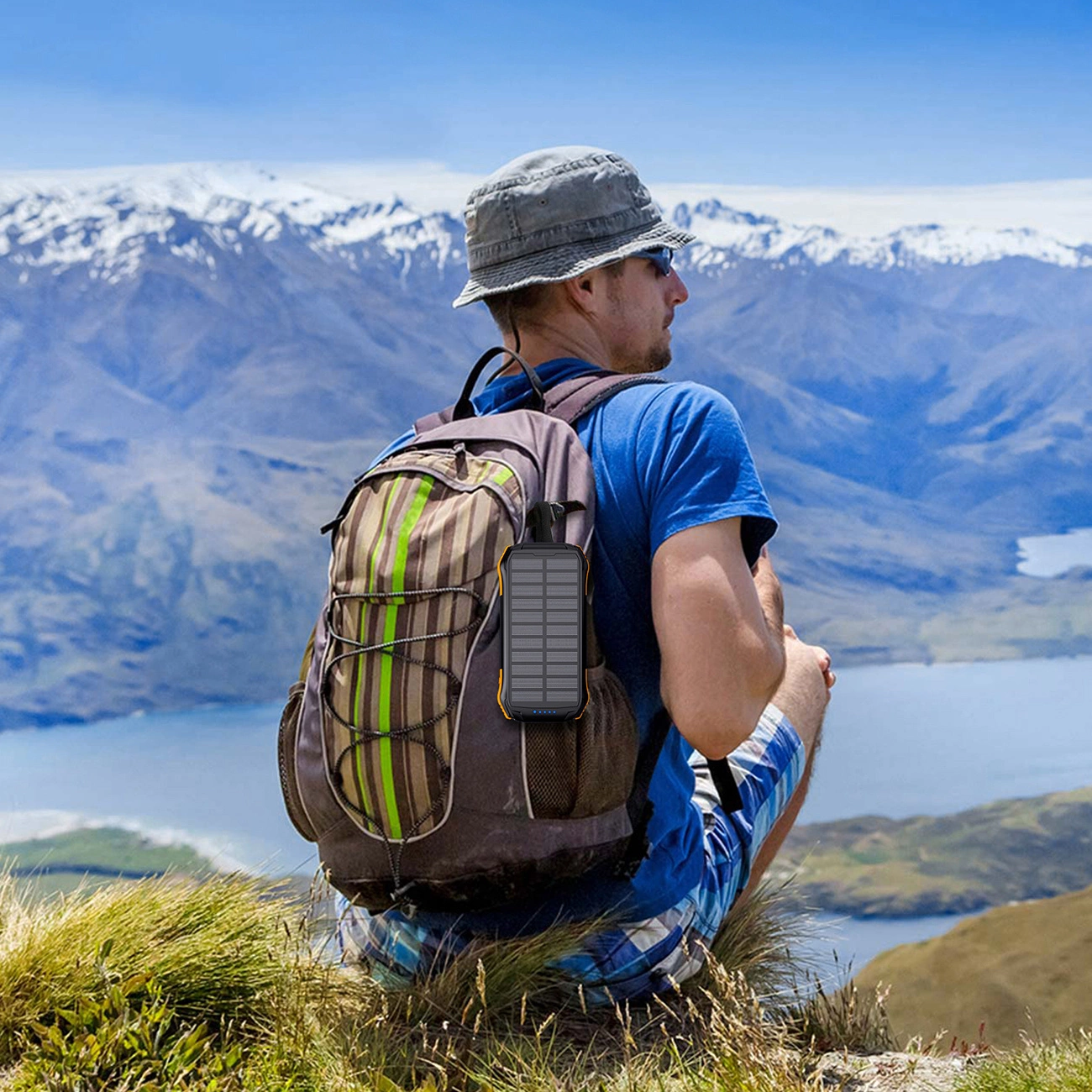 A man sitting on a hill with a Choetech B658 solar power bank attached to his backpack