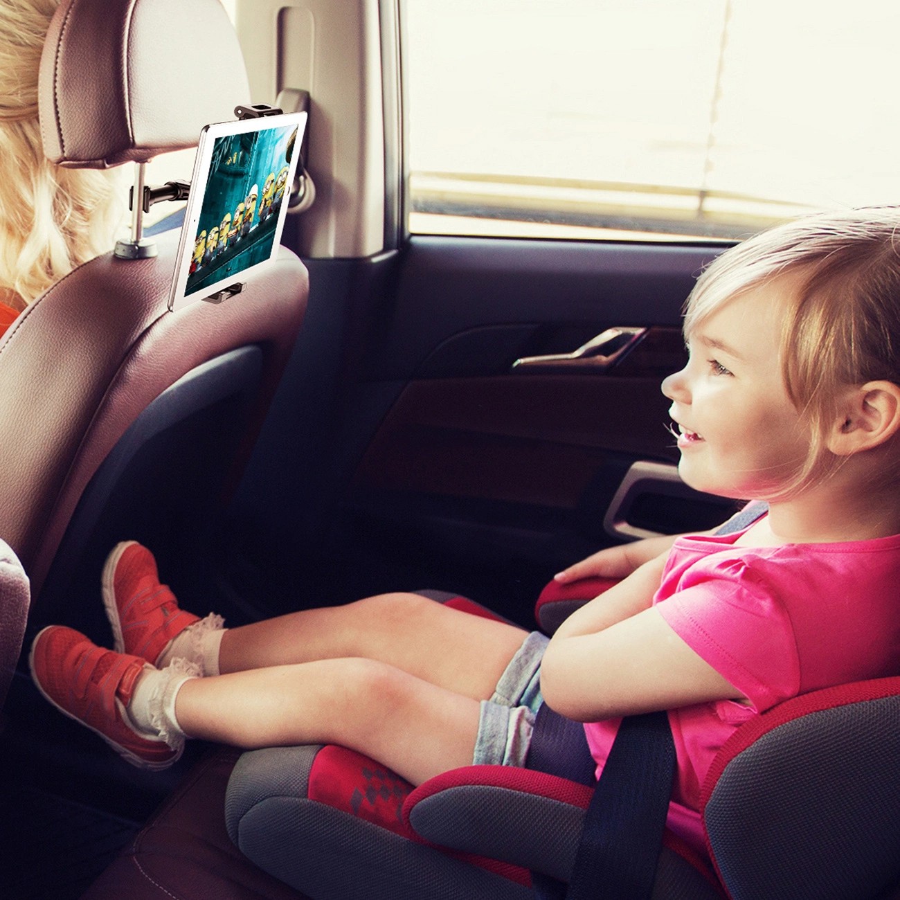 A girl sitting in a car seat watching a cartoon on a tablet placed in the Baseus Backseat Car Mount