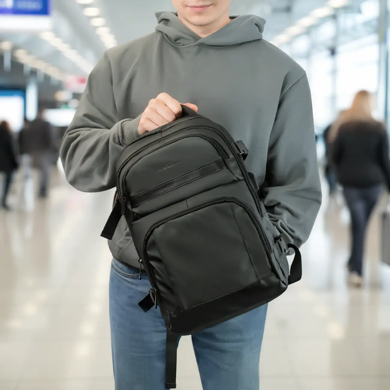 A young man dressed in casual style with a gentle smile playing on his lips holds a Wozinsky WPW-20L backpack in his hands.