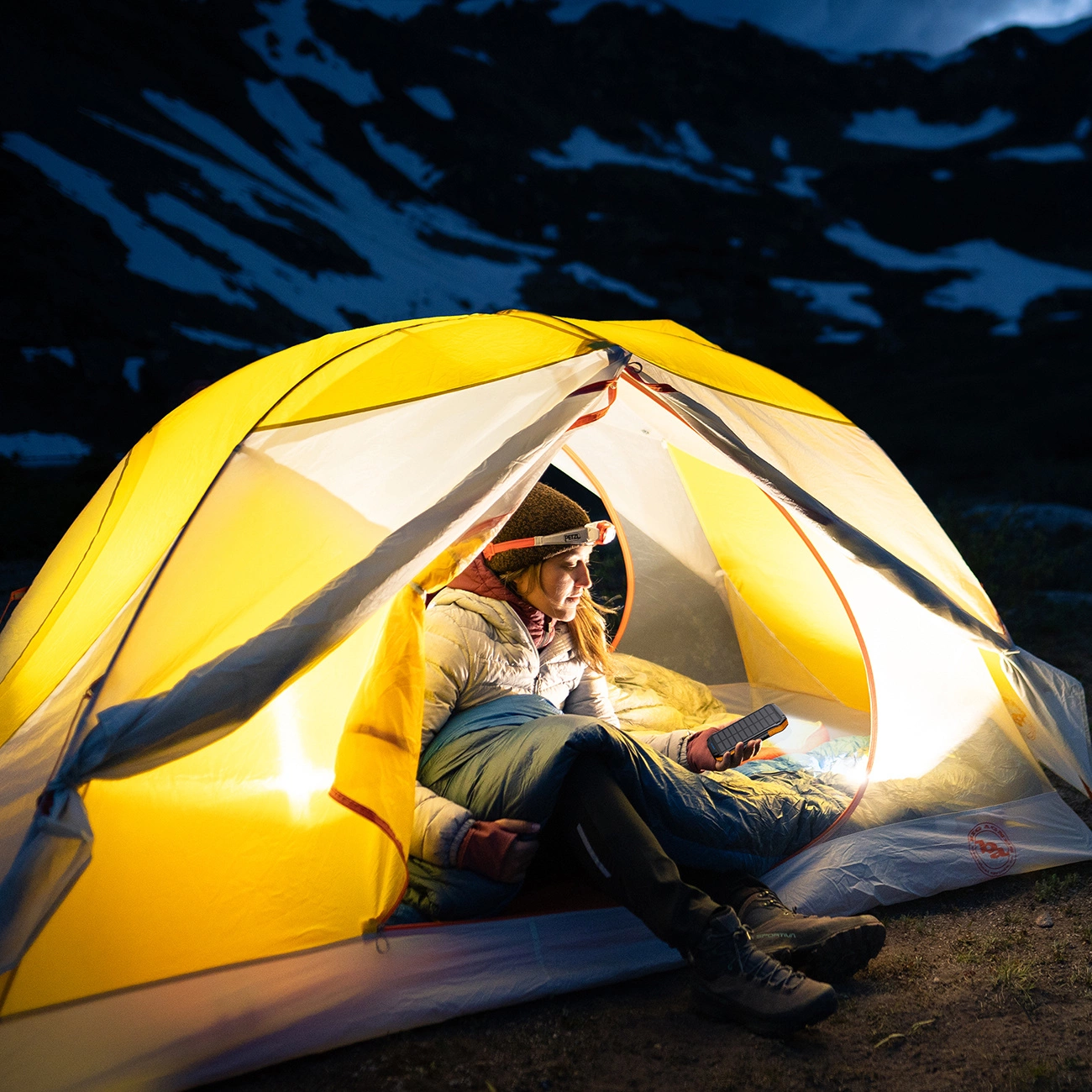 A woman sits in a tent and uses a Choetech B658 solar power bank as a lamp