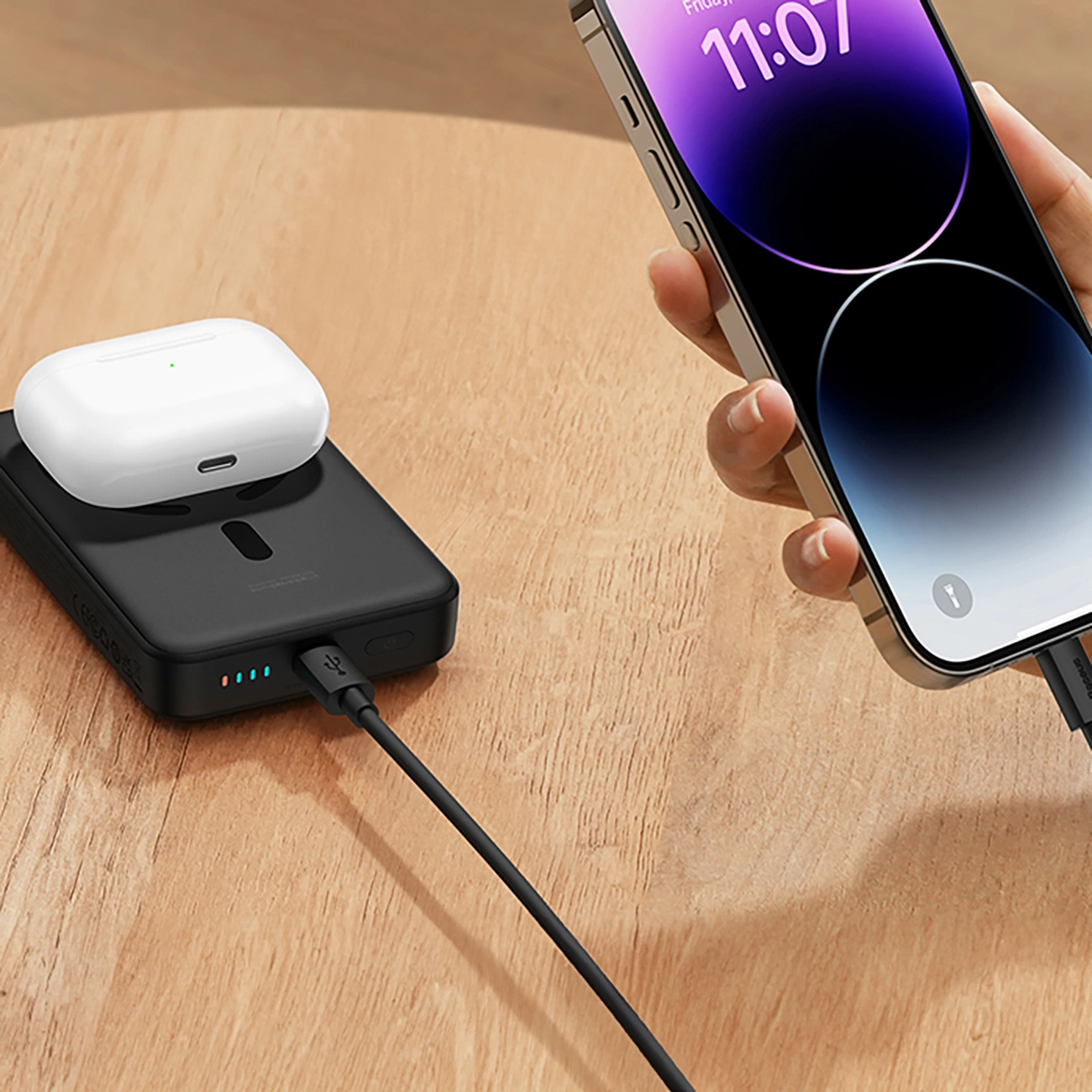 Baseus Magnetic Mini inductive 10000mAh 30W Powerbank lying on a wooden table to which the phone is connected via a cable, and inductively charging headphones lie on the surface of the Baseus Magnetic Mini Powerbank.