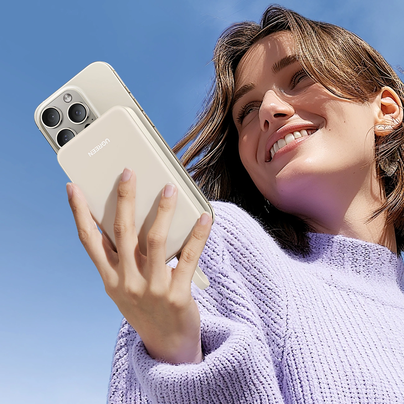 A smiling woman holds a phone with a Ugreen PB505 power bank attached